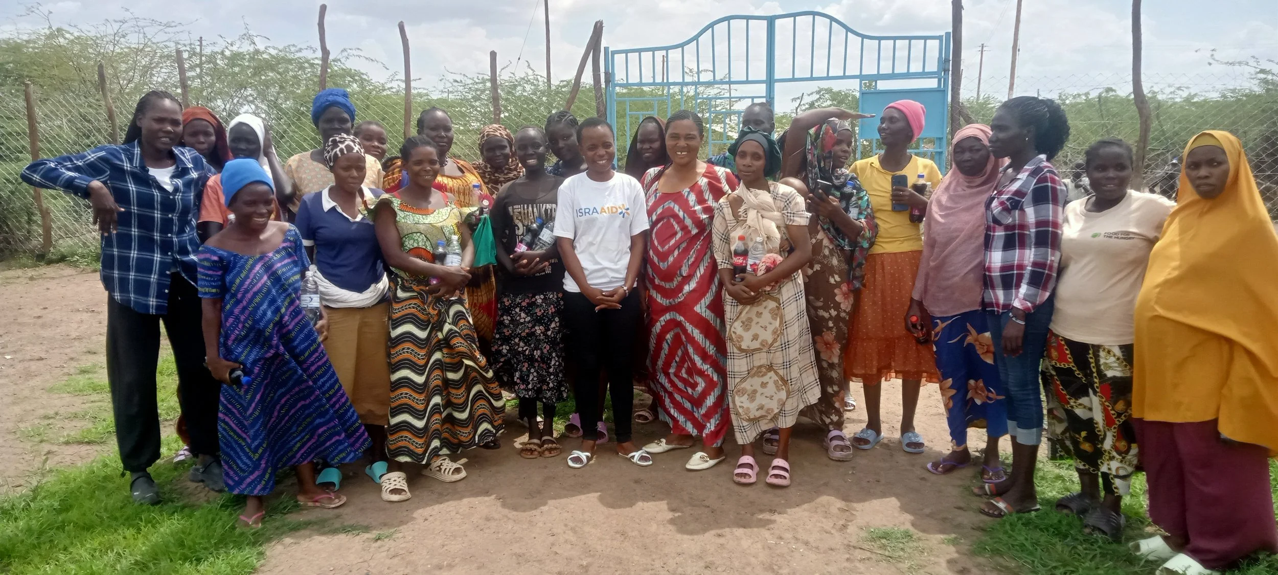 Ten people standing outdoors facing a white wall, holding up wooden plaques, with trees and a streetlamp illuminating the scene in the background.