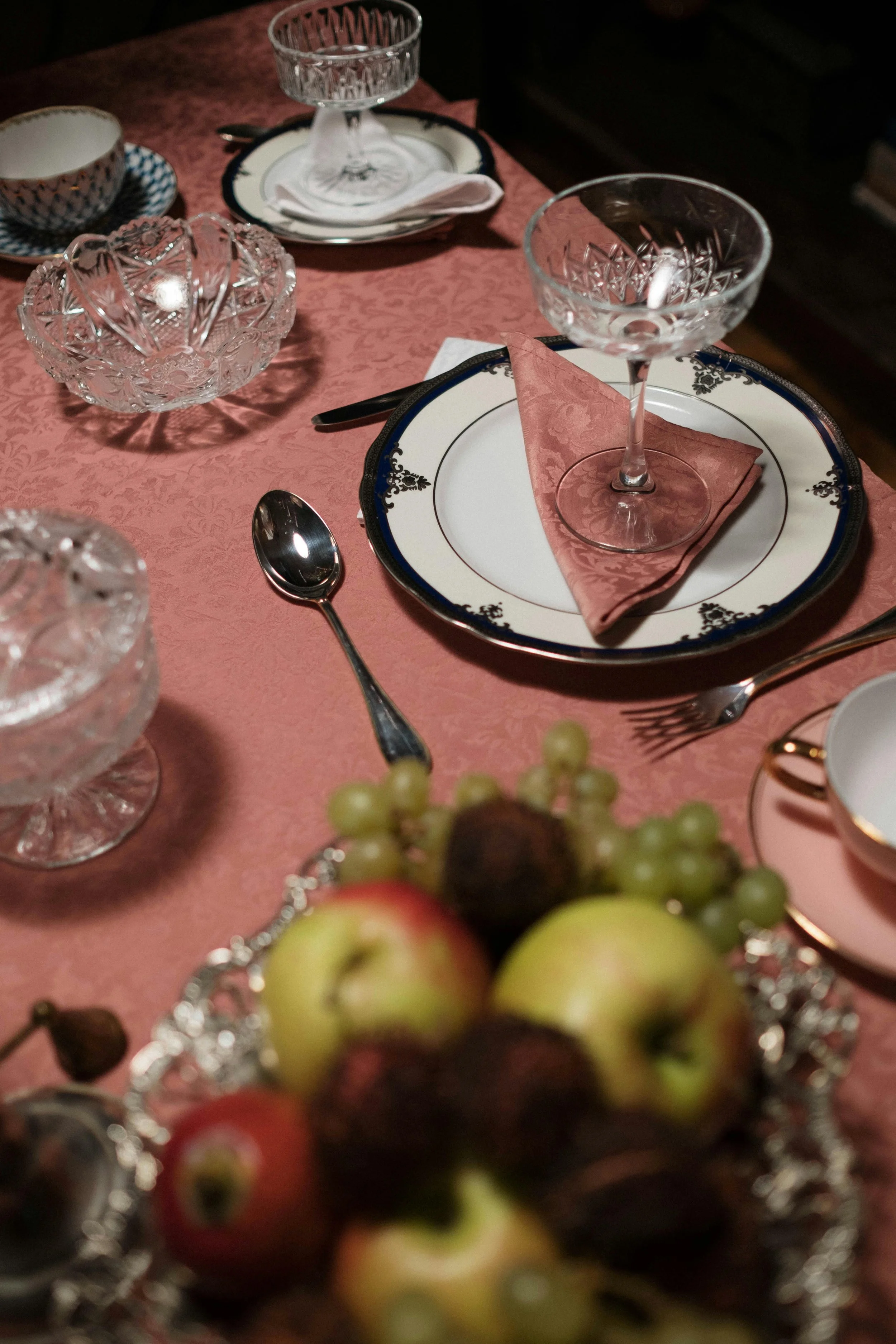 Een etentafel met elegante servies en glazen, klaar voor een maaltijd, met een vaas met fruit op de voorgrond.