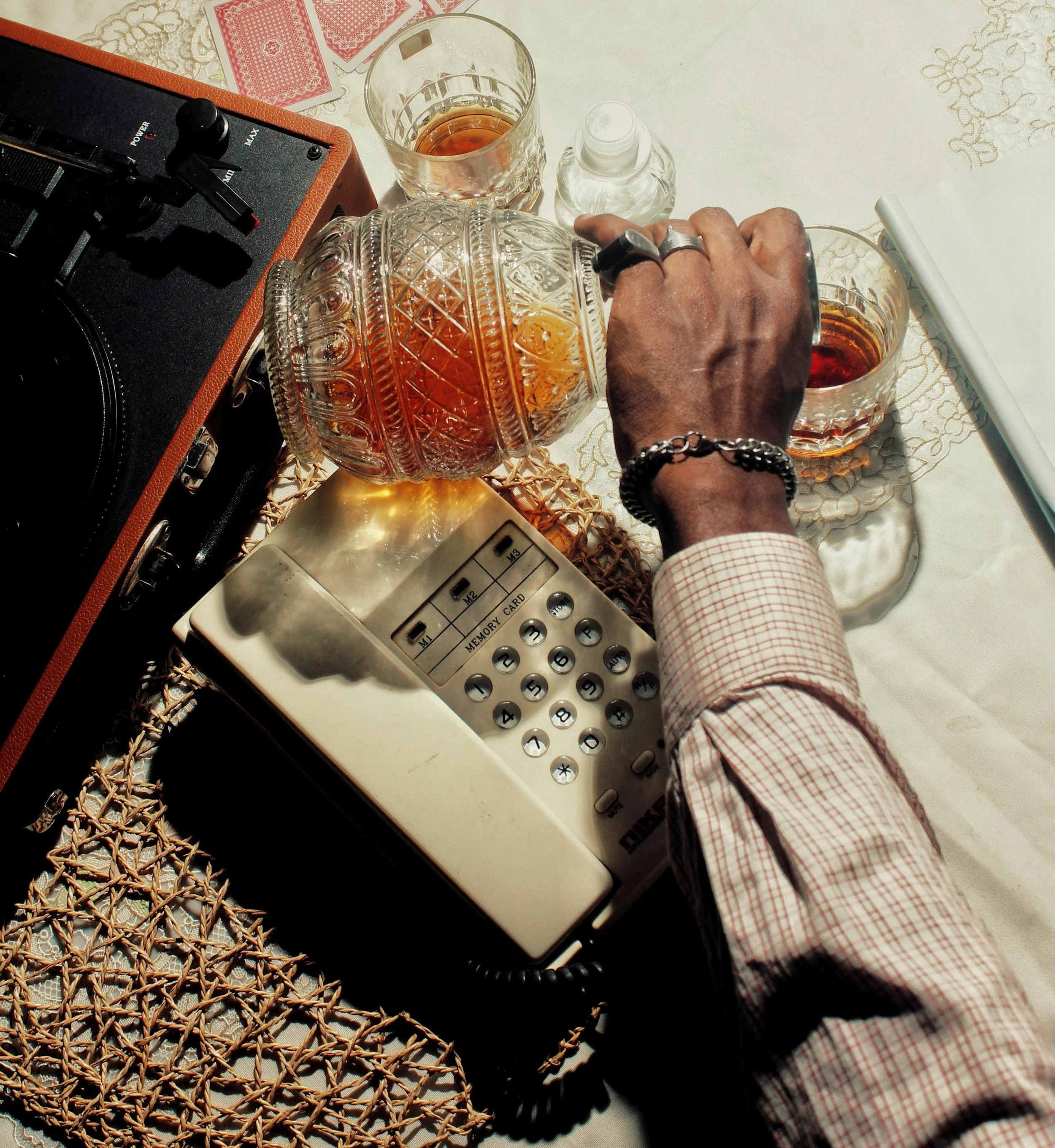 Een persoon schenkt whisky in een glas van kristal, met een tweede glas whisky en een fles op een tafel. Er ligt ook een vintage telefoon en een platenspeler op de tafel.