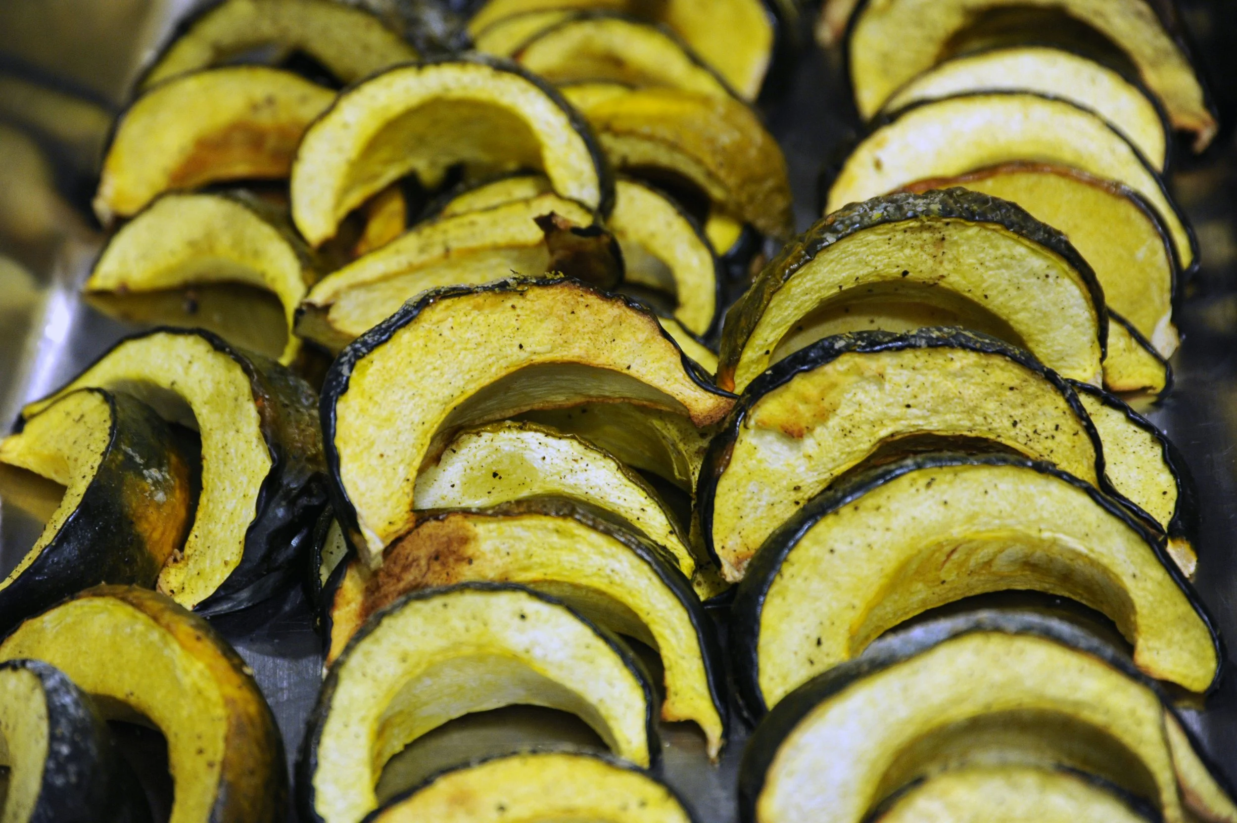 Close-up of roasted sliced yellow squash with dark edges organized on a baking sheet.