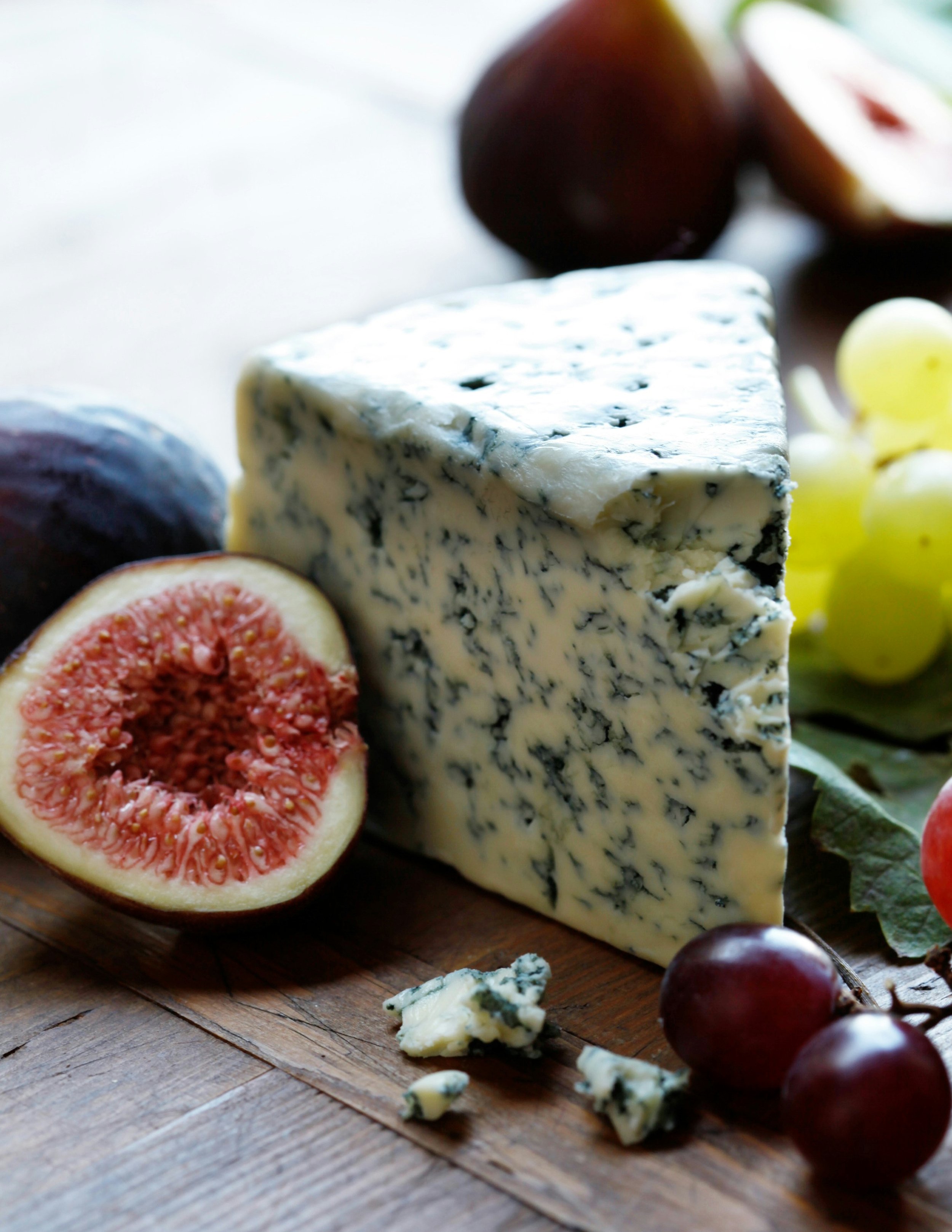 A wedge of blue cheese surrounded by ripe figs and grapes on a wooden surface.