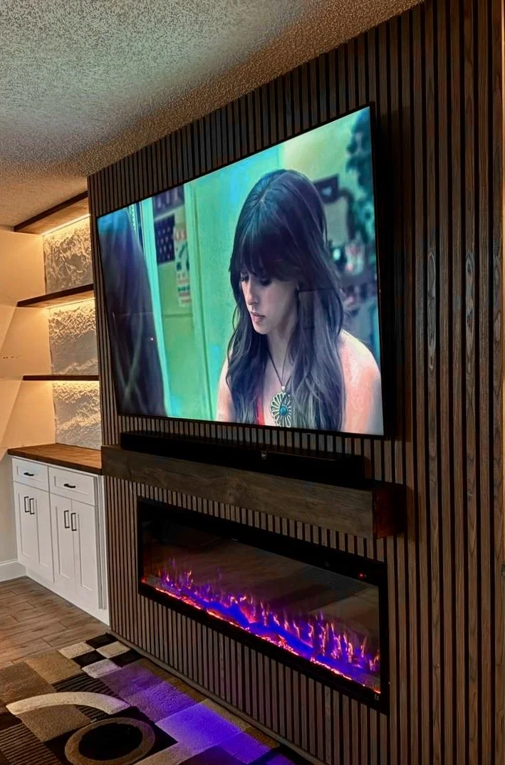 Close angled detail of a Tampa media wall showing vertical black slats, a mounted television, wood mantel, and linear electric fireplace.