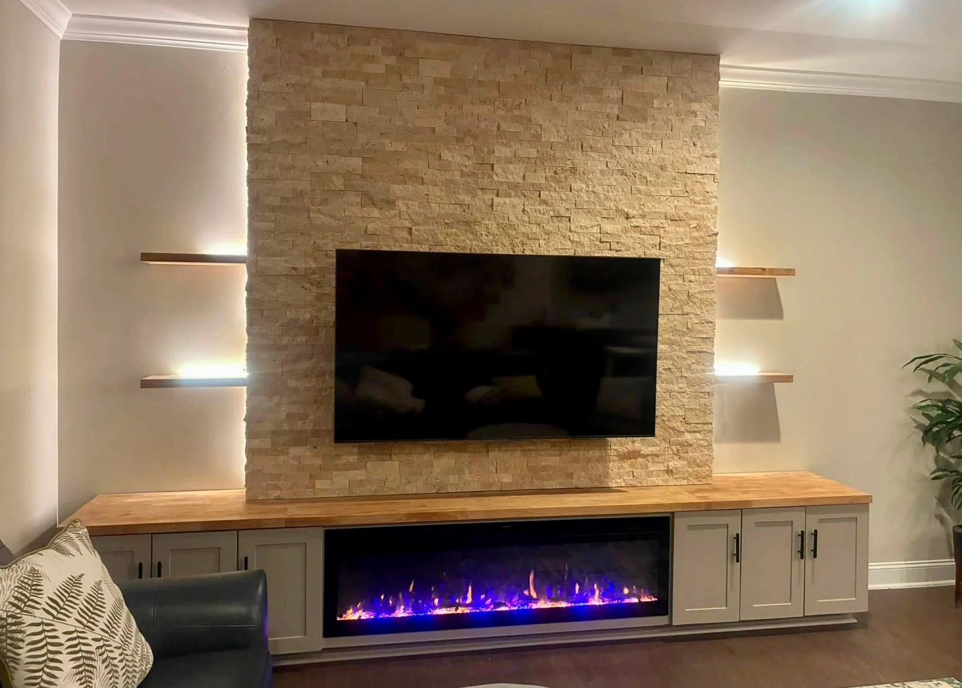 Custom entertainment built-in featuring floor-to-ceiling ledger stone, electric fireplace, closed storage, and illuminated shelves