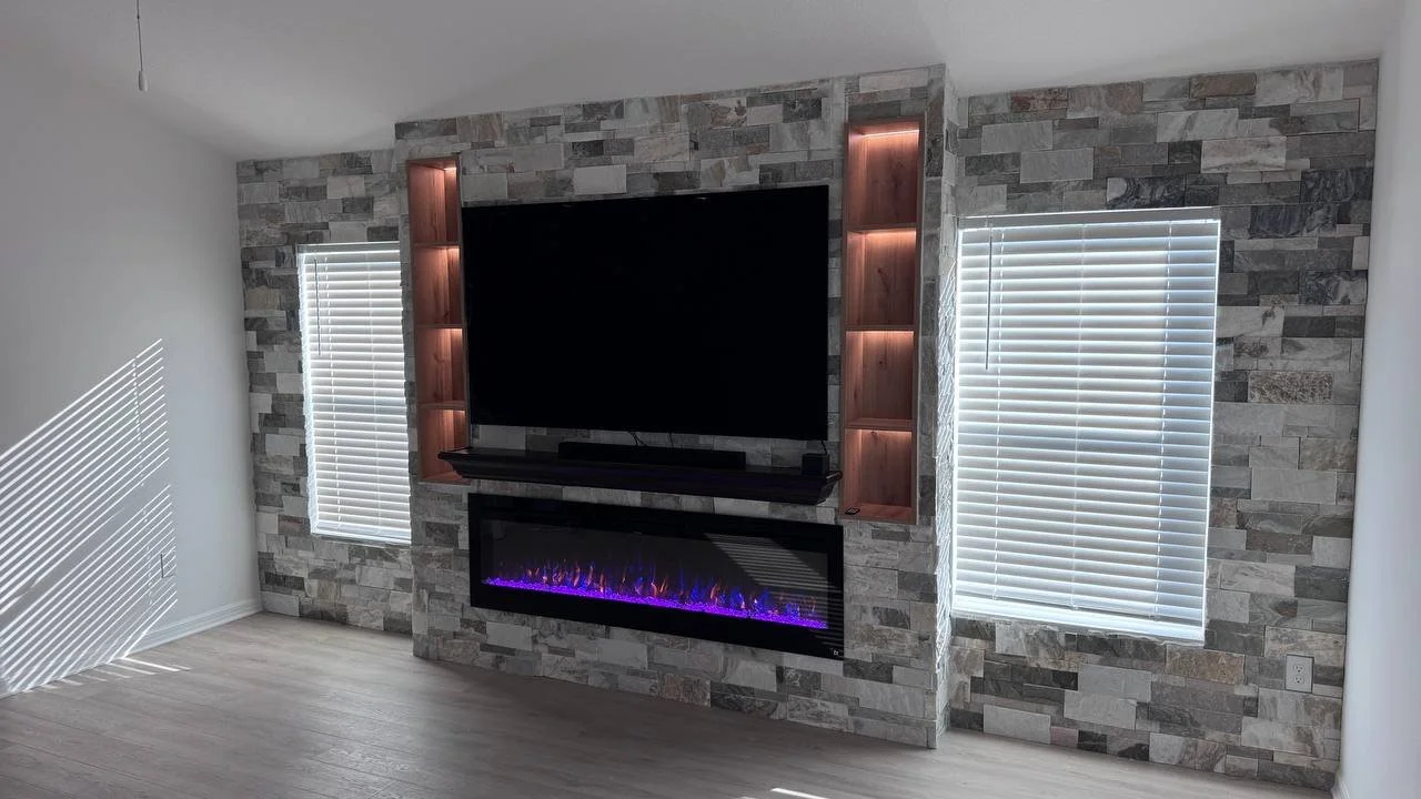 Custom stone fireplace media wall in Tampa with large TV, electric fireplace, wood mantel and illuminated niches