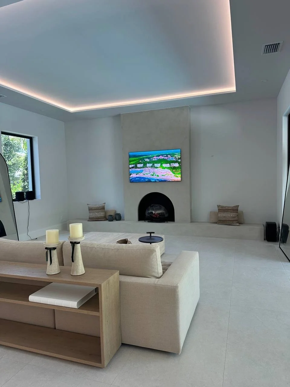 Boca Raton living room with a custom Mediterranean Hearth Wall, mounted TV, rounded fireplace, long built-in bench, and recessed ceiling lighting