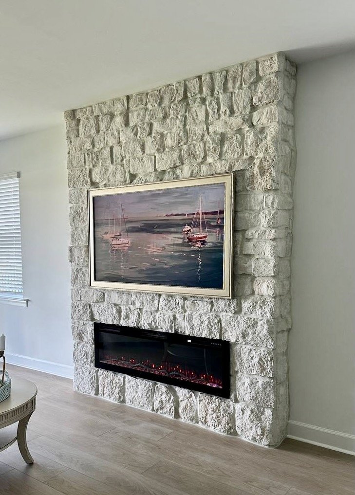 Detailed angled view of the rough white stone veneer, framed coastal artwork, and integrated linear electric fireplace.