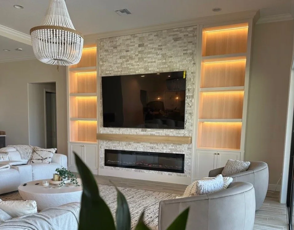 Luxury built-in media wall with LED shelves, stone center, large TV and fireplace in modern Florida living room