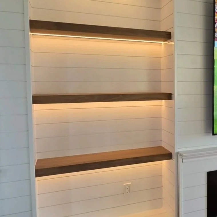 Empty built-in wall shelves with warm lighting in a room with white paneled walls.