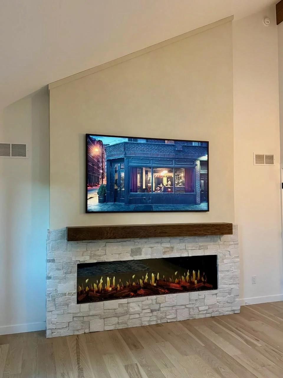 Stone and limewash fireplace media wall in Boulder, Colorado, with a dark wood mantel, mounted TV, and wide linear electric fireplace.