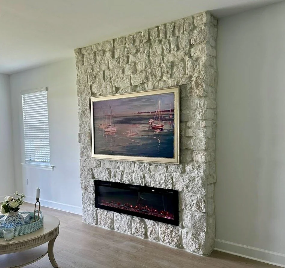 Angled view of a floor-to-ceiling white stone fireplace media wall with an electric fireplace and framed coastal artwork in Punta Gorda, Florida.