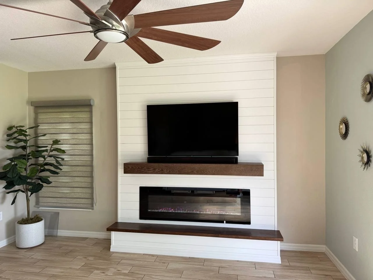 A classic build-out media wall painted white, featuring shiplap paneling, electric fireplace, and a rich wood mantel and bench, designed for a warm and timeless interior.