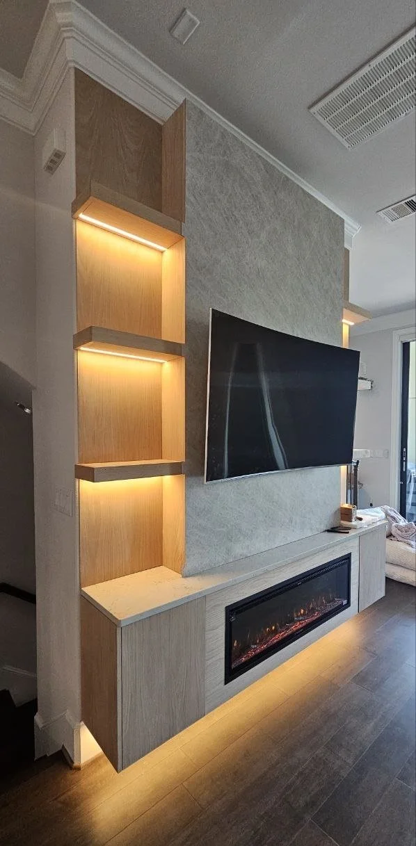 Side detail of a custom Houston media wall showing wood veneer display niches, floating shelves, concealed LED lighting, and stone-look panels