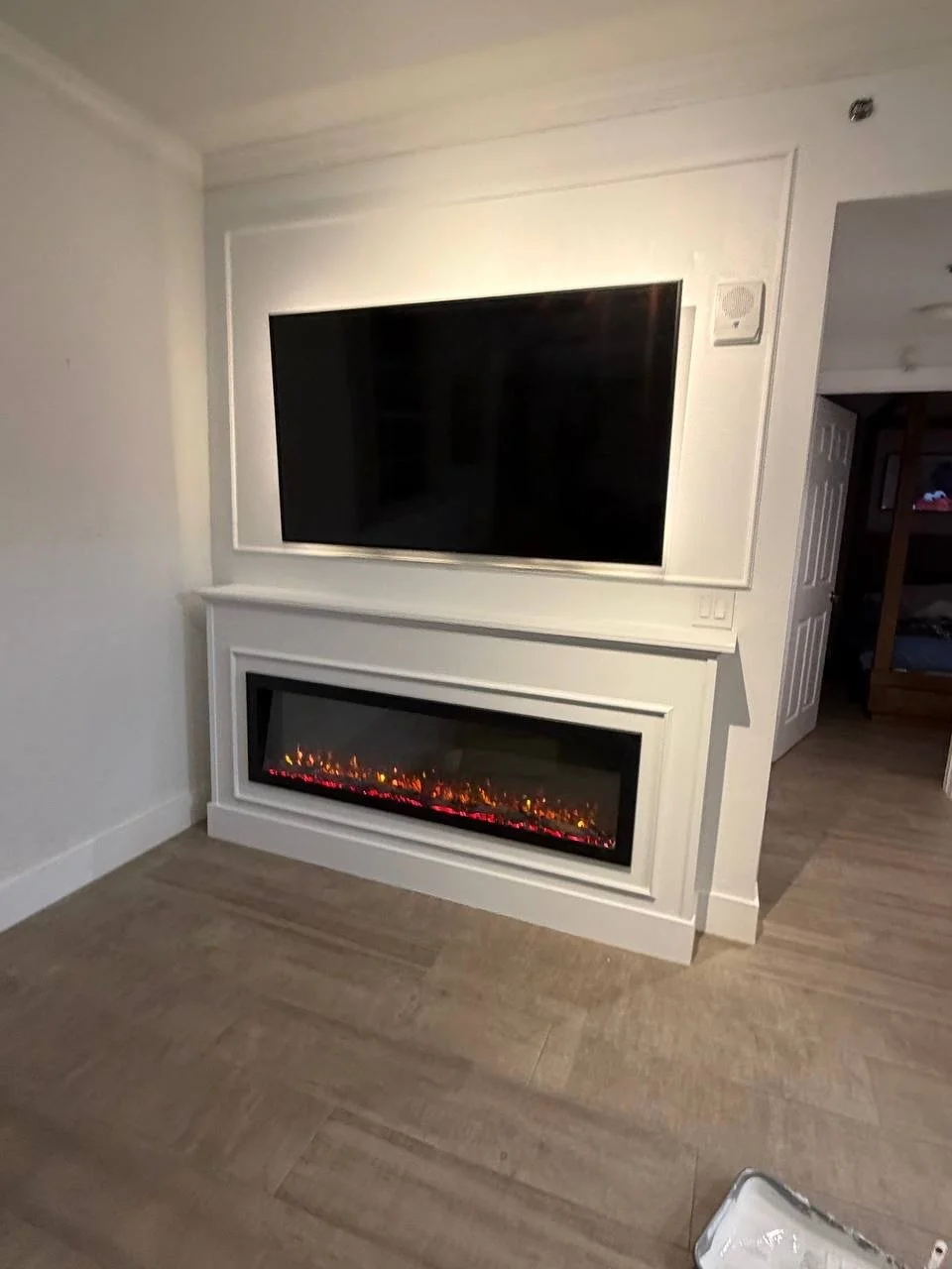 Custom fireplace media wall in Miami featuring a mounted television, warm LED backlighting, painted architectural trim, and a wide electric fireplace