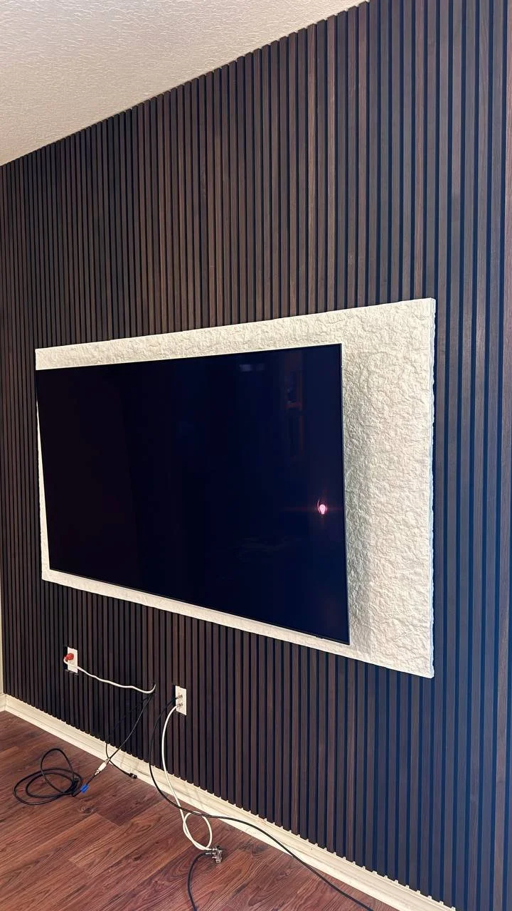 Installation progress of a custom black slat media wall showing decorative panels and textured TV surround before the floating cabinet was installed in Tampa, Florida.