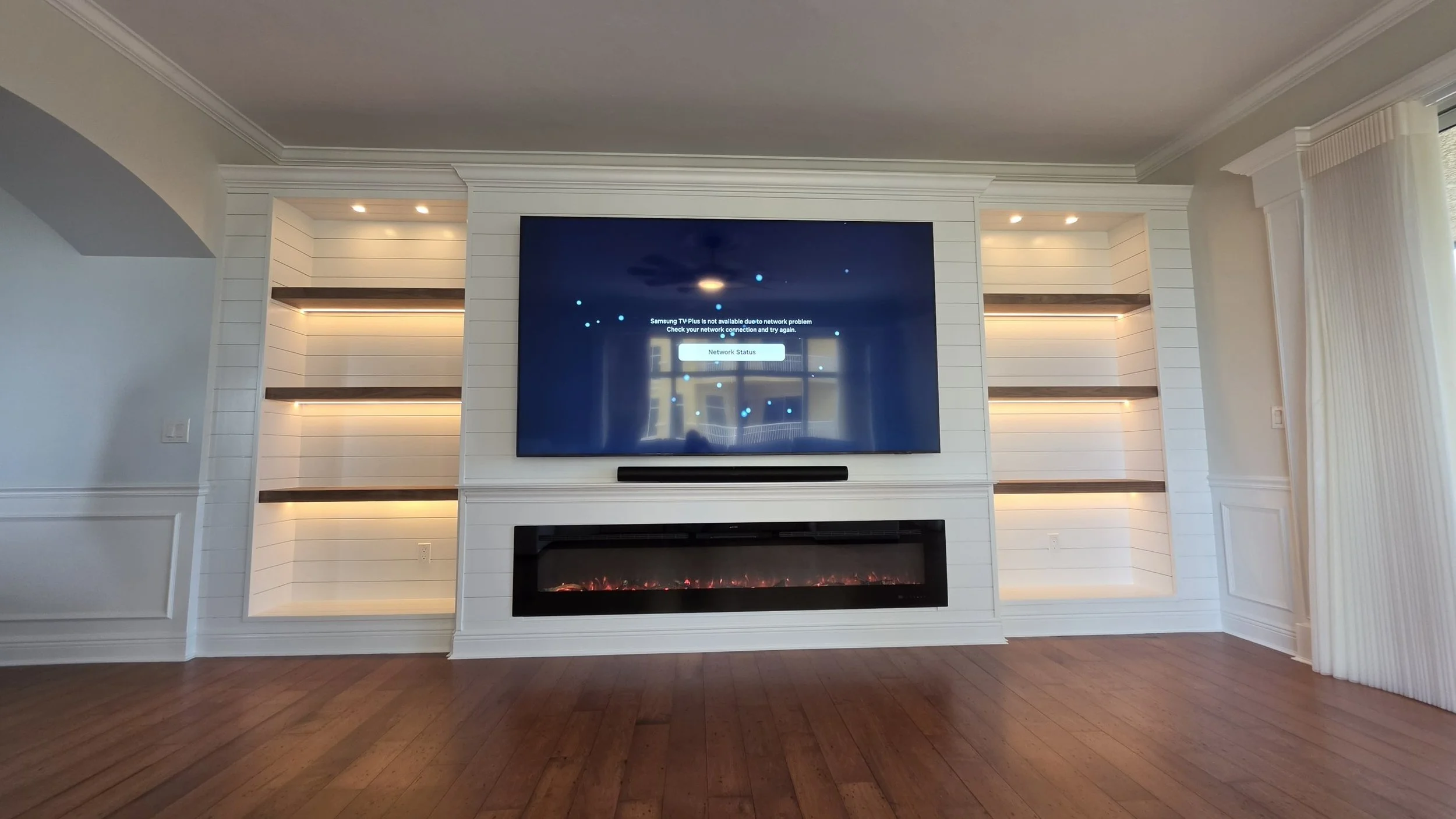 Built-in entertainment center featuring custom shiplap fireplace wall, floating wood shelves, LED lighting and linear fireplace