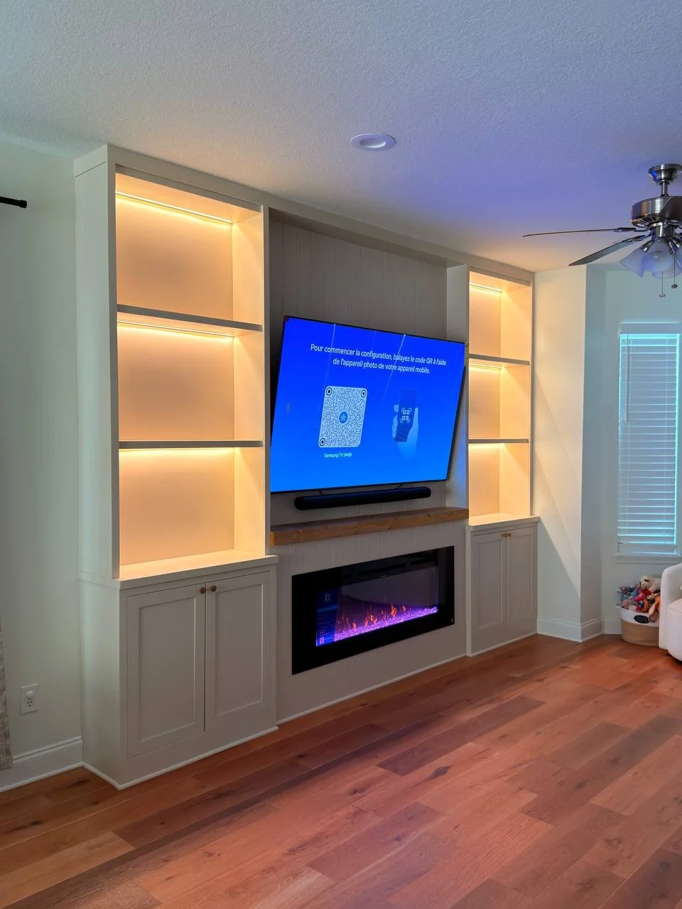 Custom entertainment built-in with electric fireplace, TV, shaker cabinets, wood mantel, and illuminated shelves in Florida.