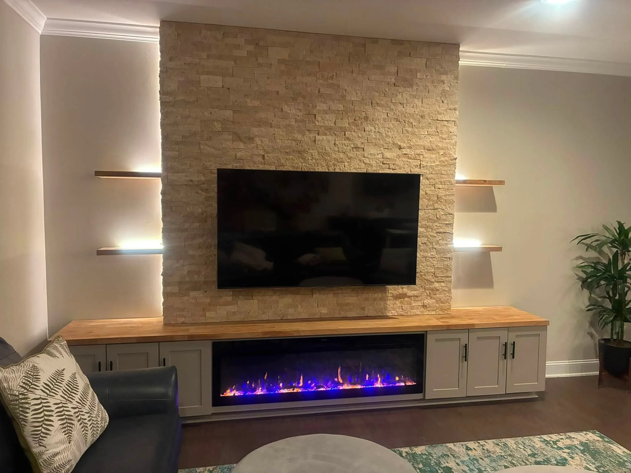 Full-width fireplace media wall with ledger stone, 60-inch electric fireplace, gray storage cabinets, and wood countertop