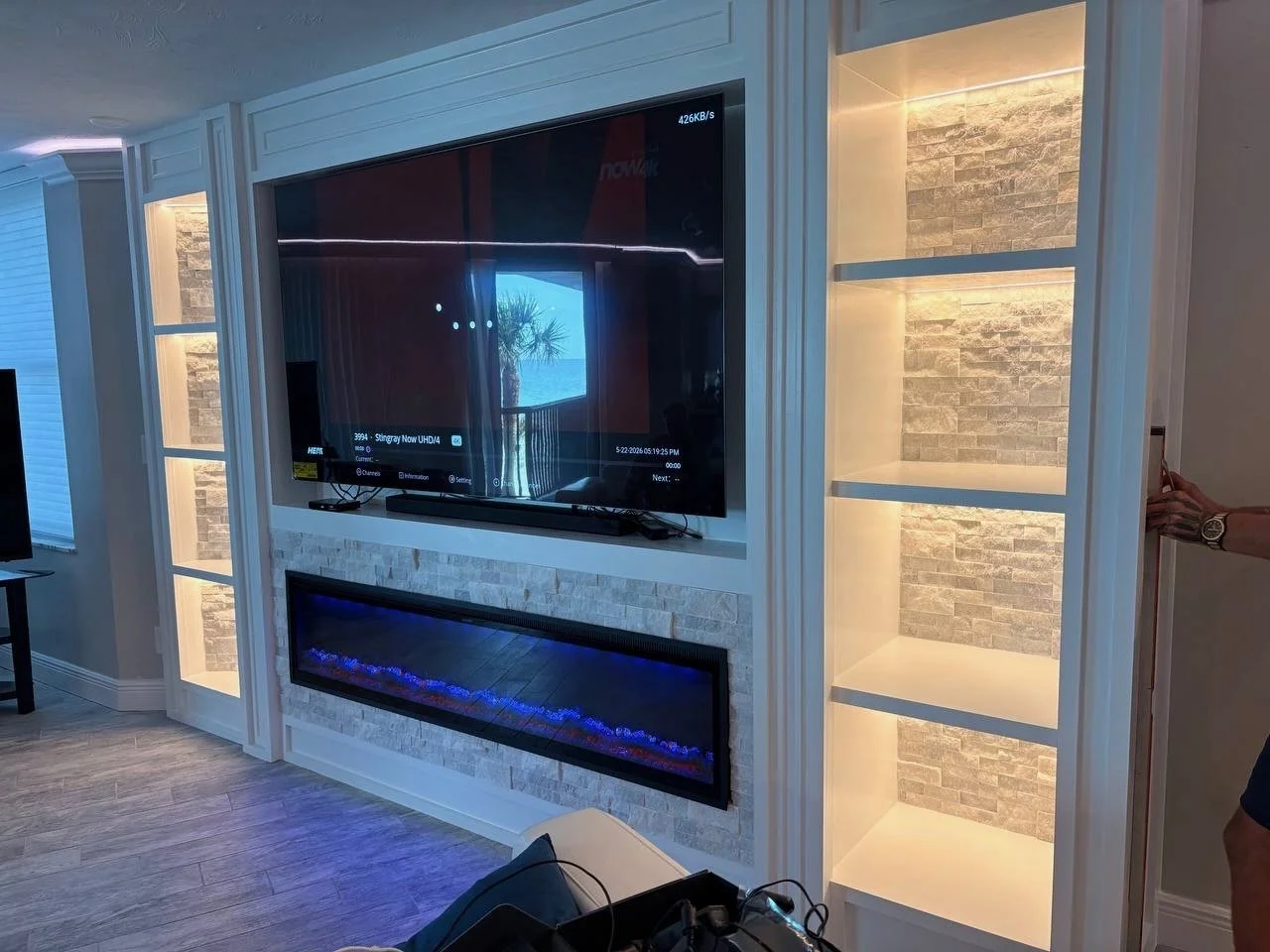 Luxury stone fireplace media wall with illuminated display niches and recessed TV design in Florida home