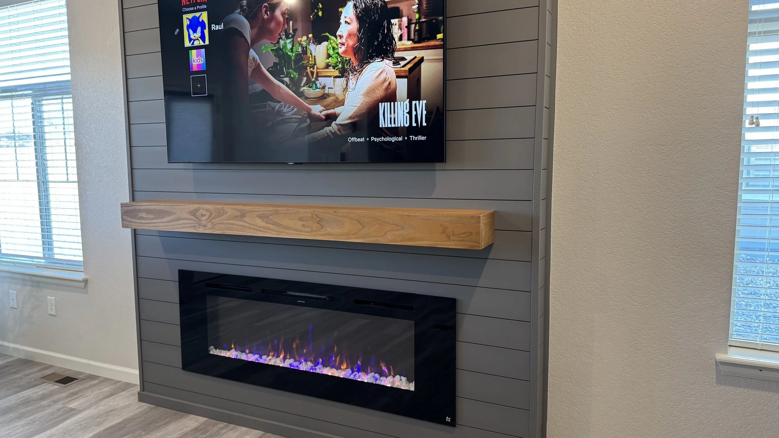 natural wood mantel beam installed above electric fireplace on dark shiplap media wall