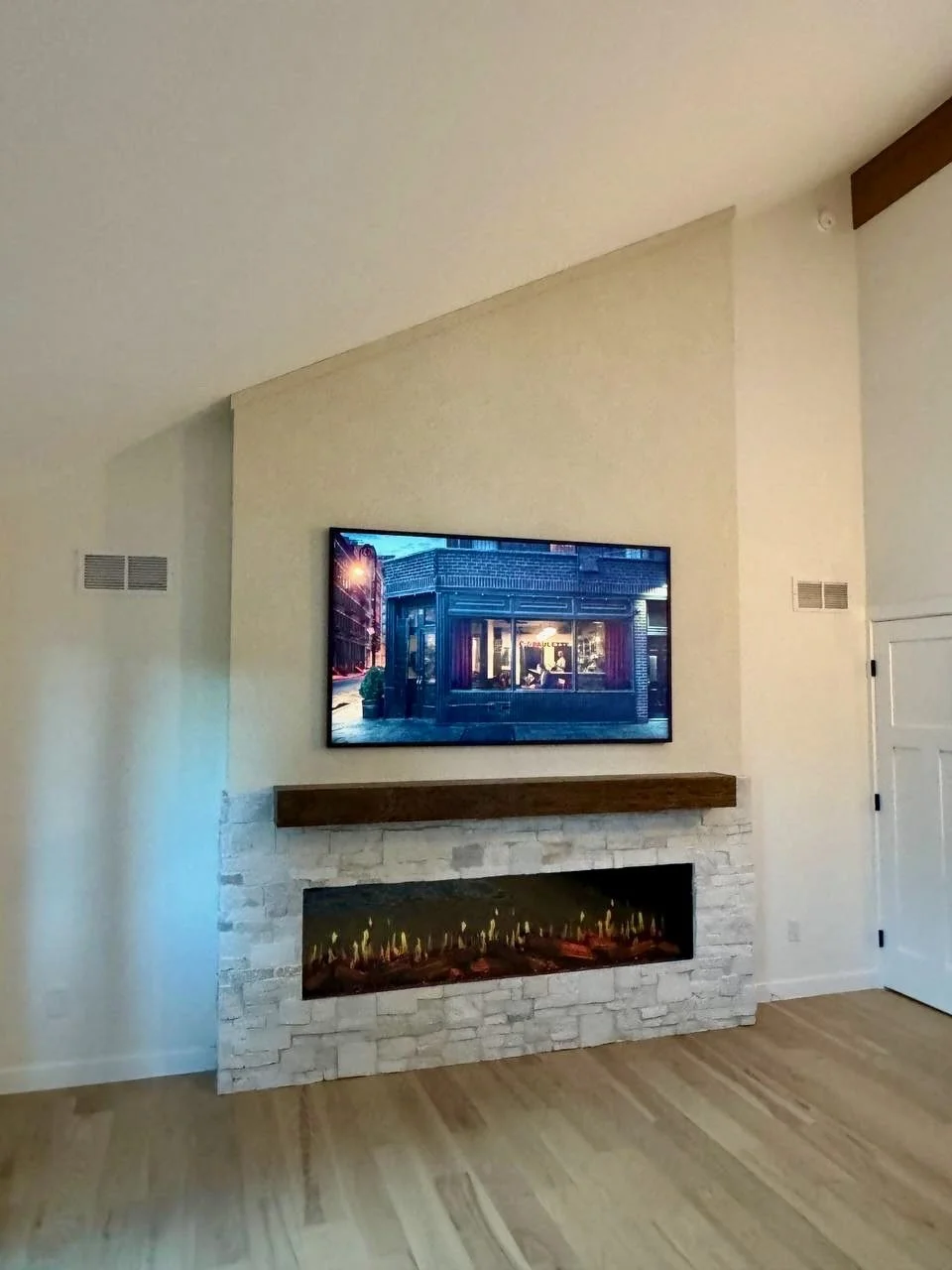 Completed hybrid fireplace media wall in Boulder combining a sloped limewash upper section, stone base, wood mantel, and linear fireplace.