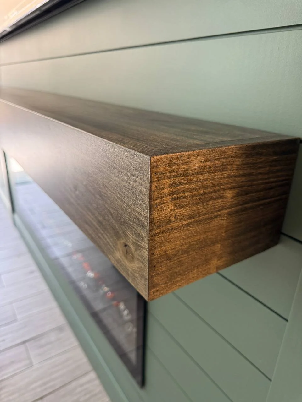 Close-up of a dark-stained natural wood mantel installed on a green shiplap fireplace wall.