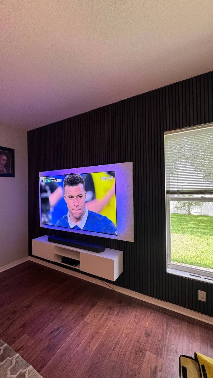Angled view of a contemporary black slat media wall with floating cabinet and textured TV panel installed in a Tampa, Florida home.