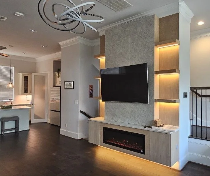 Completed custom entertainment wall in a Houston living room with integrated fireplace, television, floating cabinetry, shelves, and ambient lighting