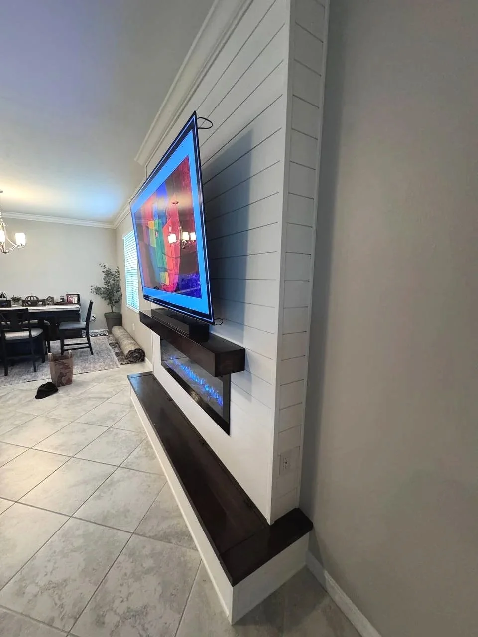 Side view of a built-out shiplap fireplace media wall in Houston showing finished returns, mounted TV, wood mantel, electric fireplace, and lower bench.