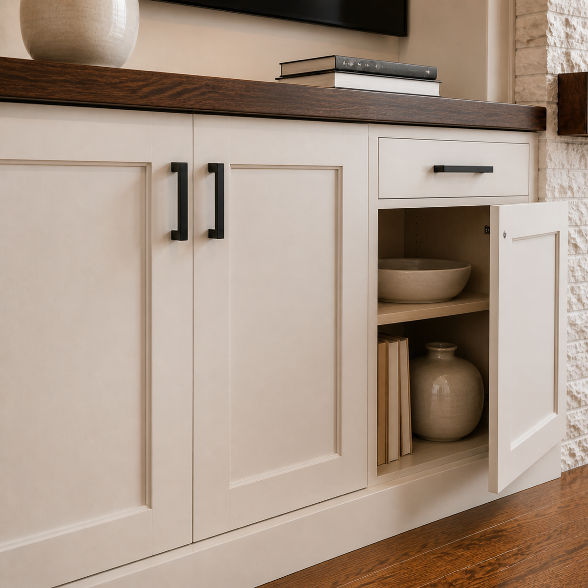 Close-up of a kitchen cabinet with a partially open door revealing decorative bowls and books inside, with a wooden countertop on top.