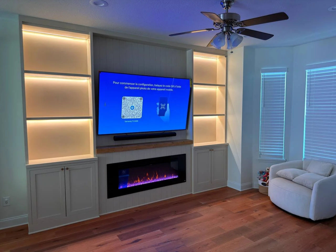 Custom entertainment built-in with electric fireplace, TV, shaker cabinets, wood mantel, and illuminated shelves in Florida.