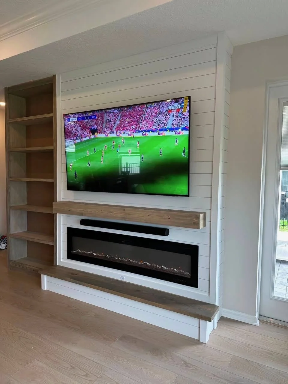 Custom white shiplap media wall with wall-mounted TV, electric fireplace, floating wood mantel, and built-in shelving