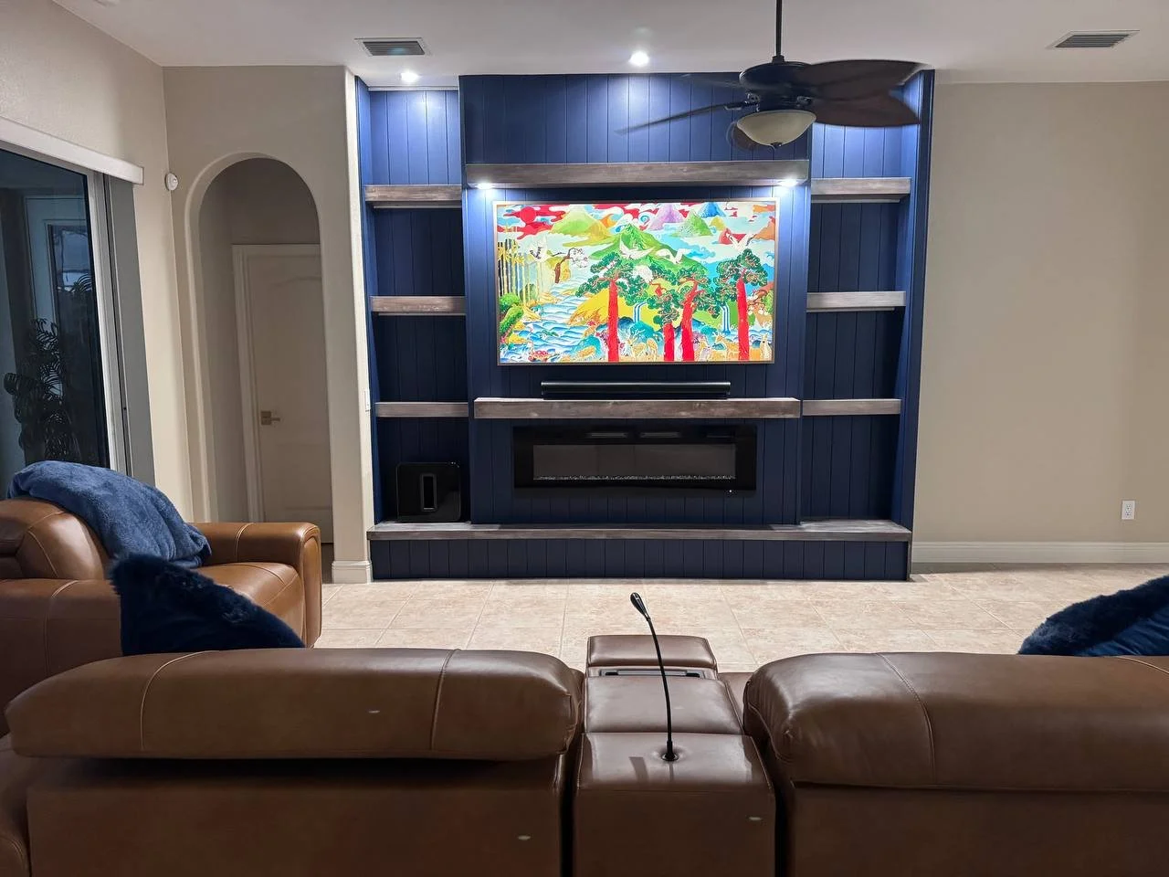 Full living-room view of a navy shiplap fireplace media wall with symmetrical niches, integrated lighting, wood shelves, and a mounted television in Dallas, Texas.