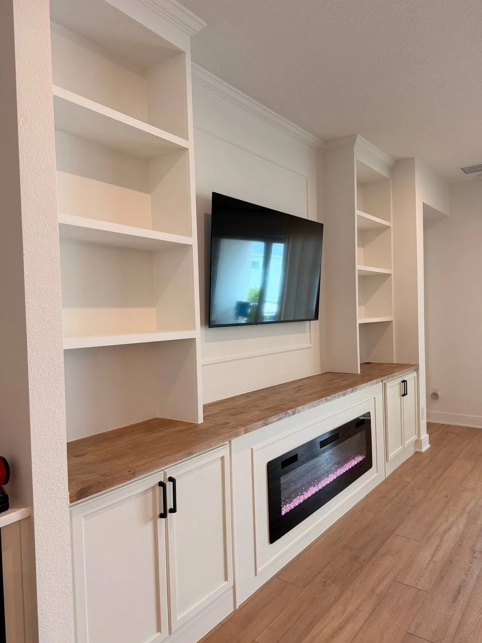 Angled view of a Tampa fireplace media wall with shaker cabinets, open display shelves, wood countertop, mounted television, and electric fireplace