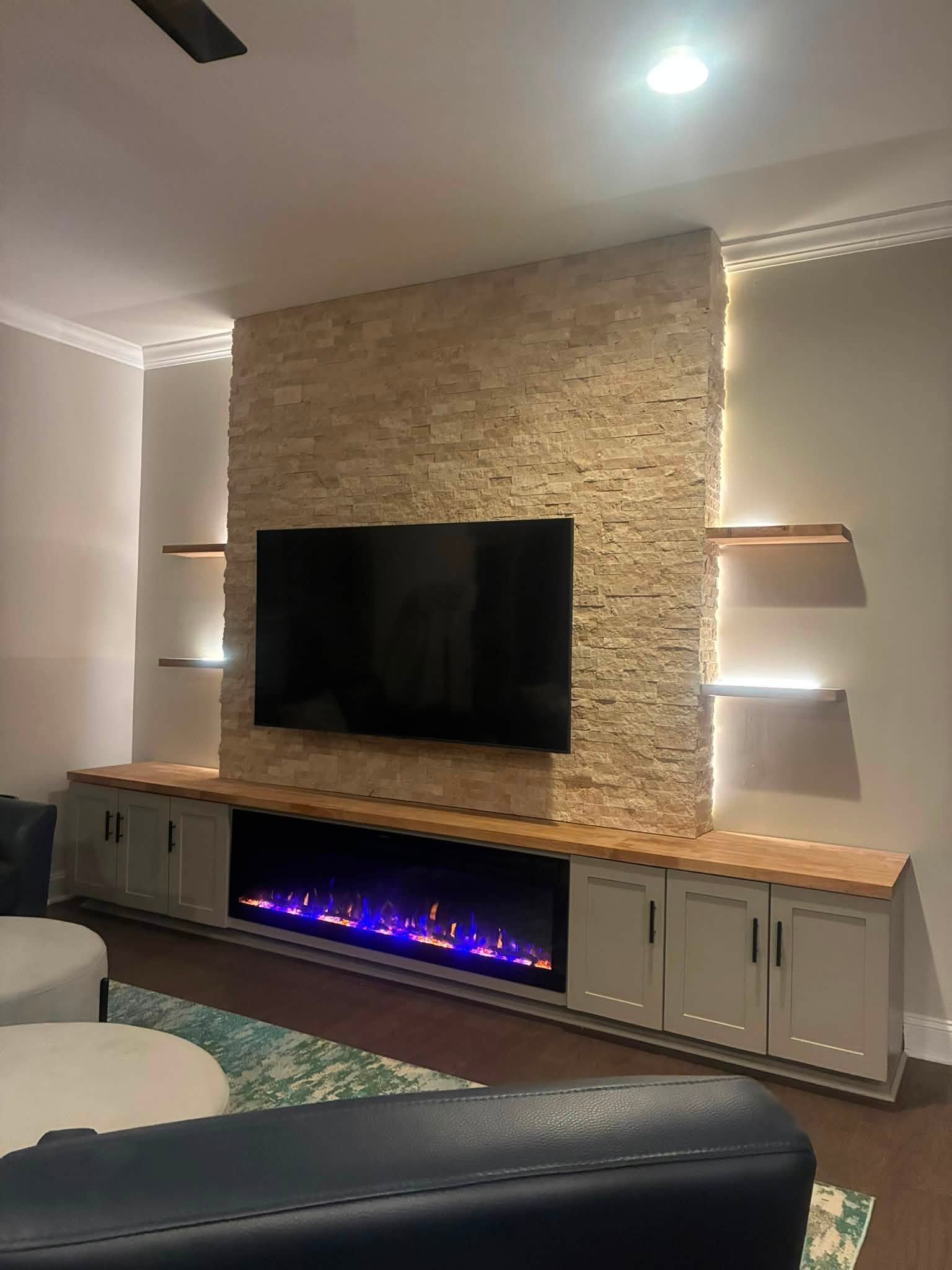 Completed ledger stone fireplace media wall with floating shelves, LED lighting, custom cabinets, and mounted TV in Durham, NC