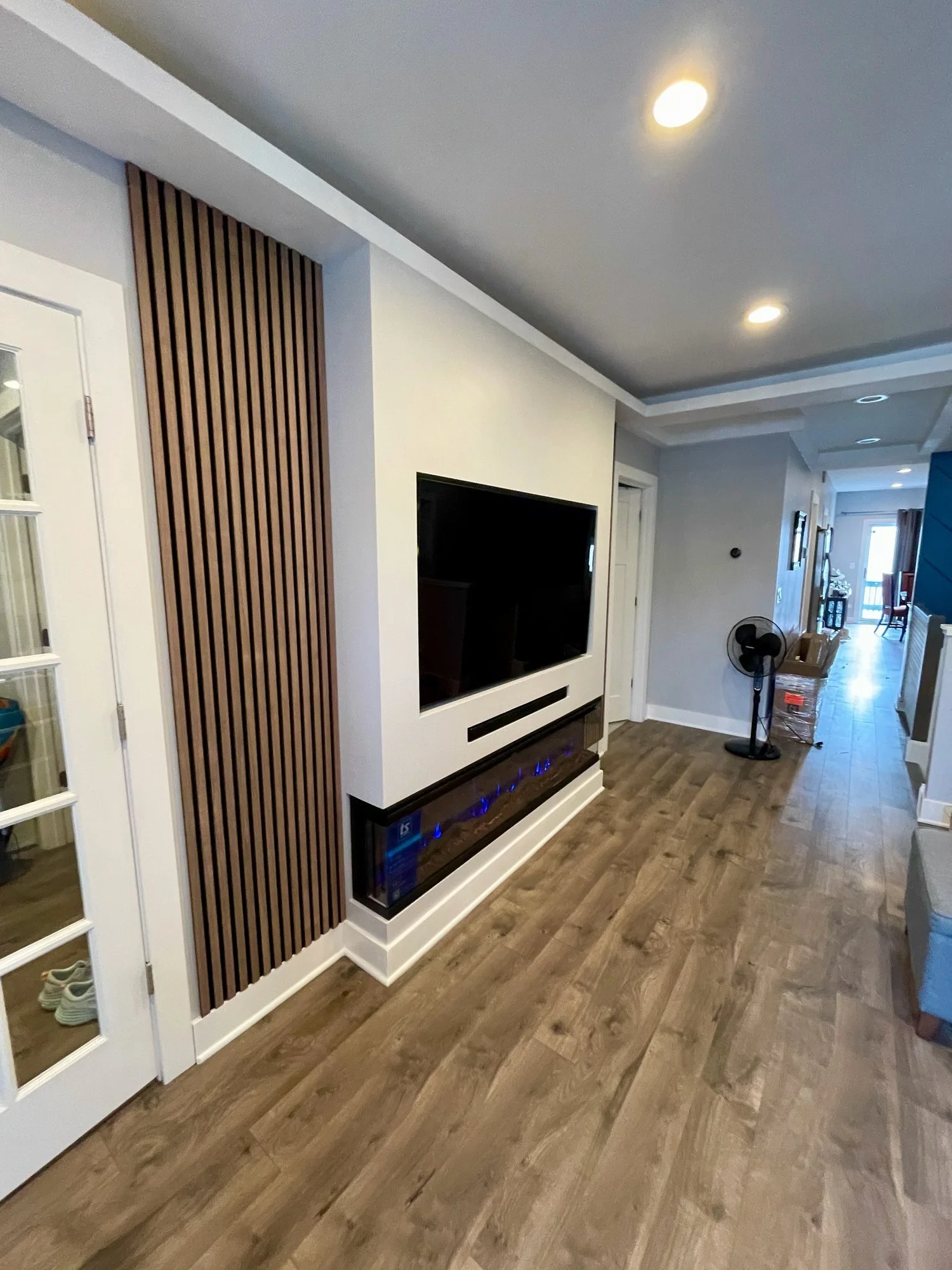Angled view showcasing depth and detail of fireplace glass, mounted TV, and vertical wood slat side panels.