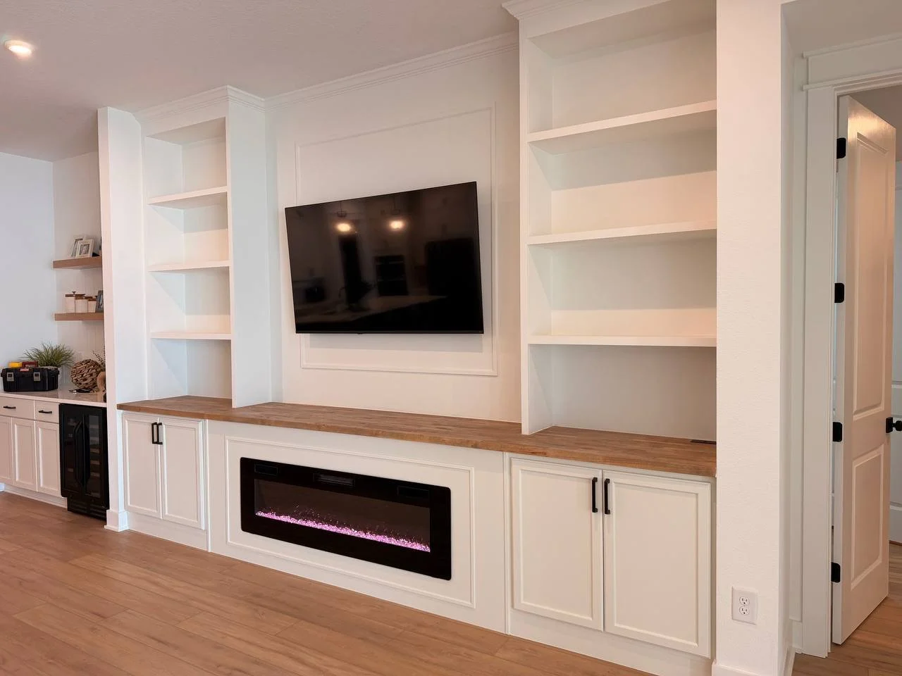 Classic white built-in TV wall in Tampa featuring symmetrical shelving, concealed storage, architectural trim, and a linear electric fireplace