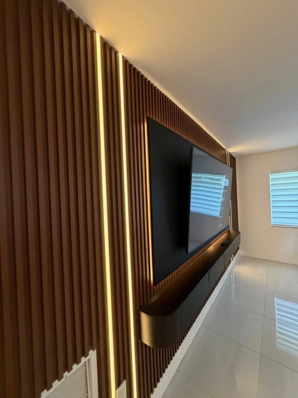 Side detail of wood-look decorative slats, vertical LED lighting, a dark TV panel, and a floating media cabinet in a Miami-area home.