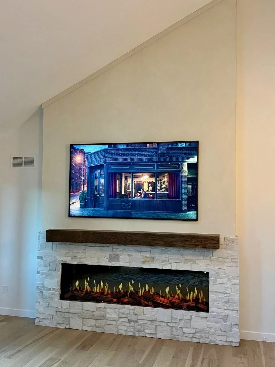 Light stone fireplace surround beneath a dark wood mantel, with a mounted television against the warm limewash wall above.