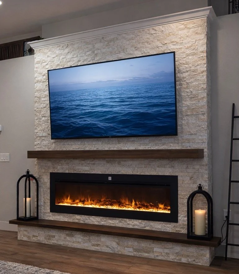 Living room with a stone fireplace, a large flat-screen TV displaying an ocean scene mounted above the fireplace, and two lanterns with candles on dark wooden shelves on either side.