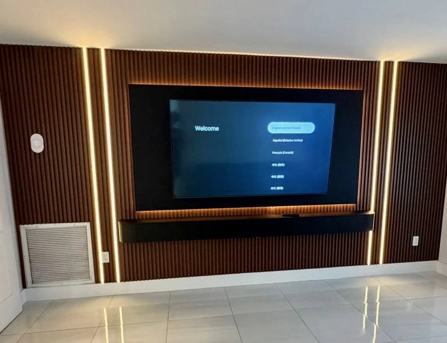Wide view of a Miami-area media wall with full-width vertical slat panels, a mounted TV, warm accent lighting, and a floating cabinet.
