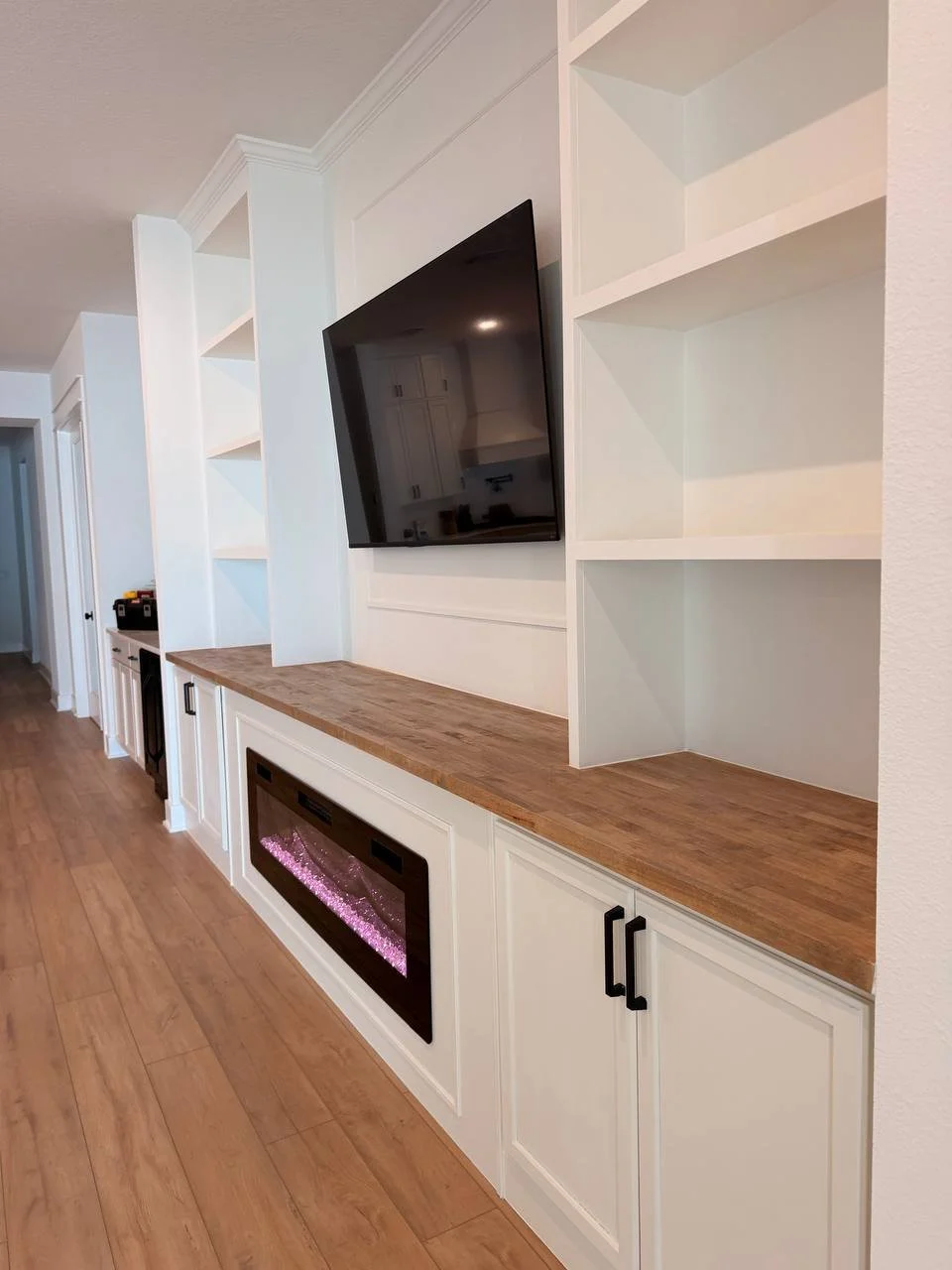 Side detail of custom white cabinetry, open shelving, stained wood countertop, TV panel molding, and electric fireplace in a Tampa home