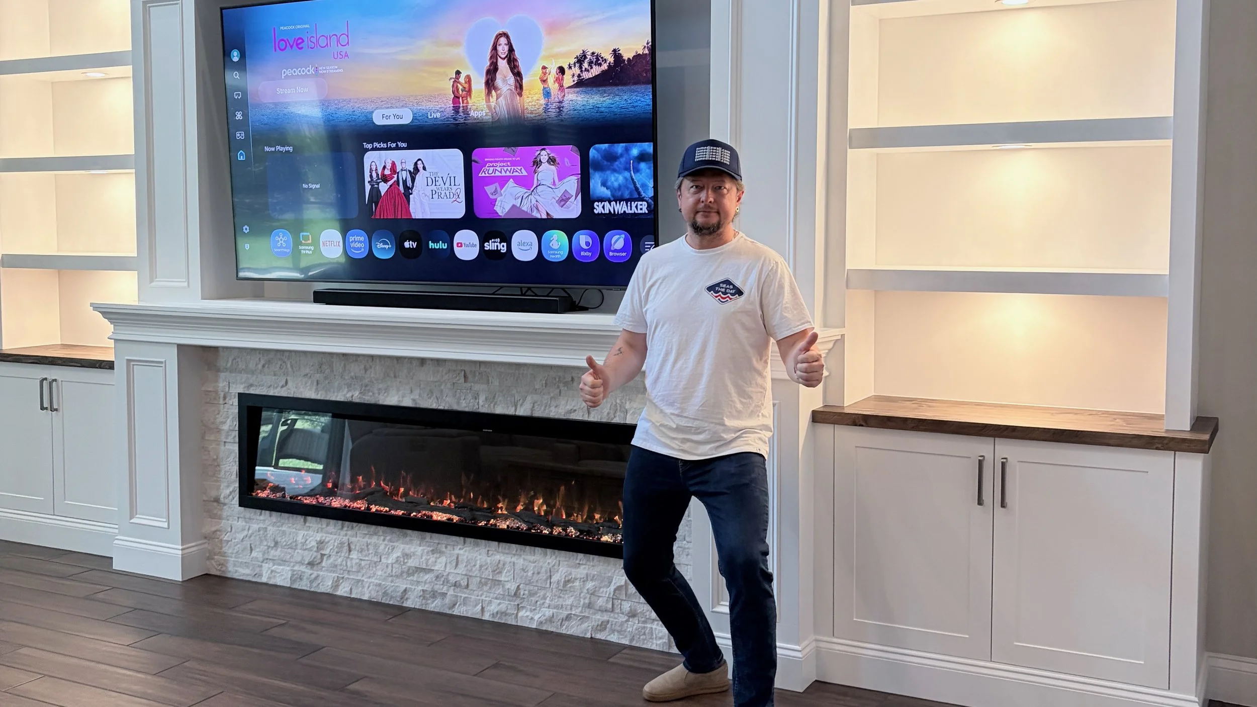 Evgeny standing beside a completed fireplace media wall with custom cabinetry, illuminated shelves, and mounted TV