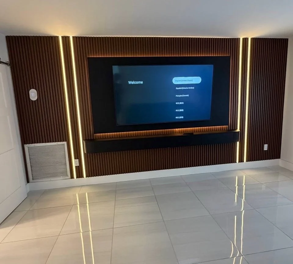 Modern TV wall in the Miami area with warm wood-look slat panels, a dark TV surround, vertical LED lighting, and a long floating media cabinet.