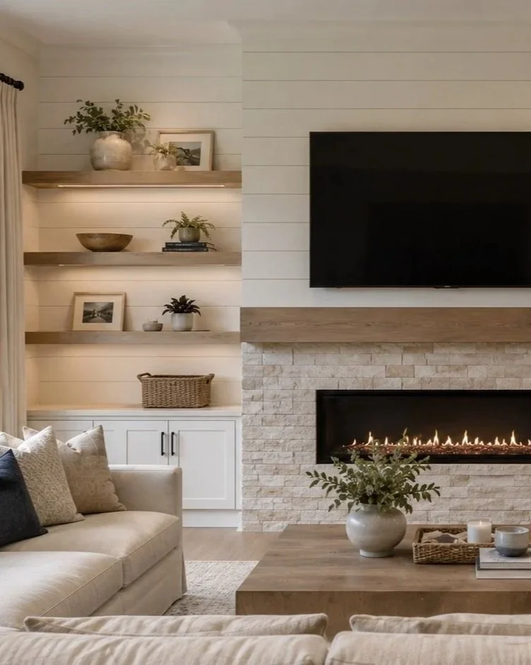 Living room with beige sofa, beige pillows, fireplace with a modern design, white shiplap walls, and mounted flat-screen TV. Shelves with decorative items, framed photos, plant pots, and a basket.