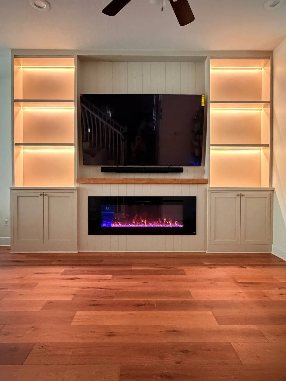 Custom built-in media wall in Central Florida with a large television, electric fireplace, vertical panel detailing, and wood mantel.