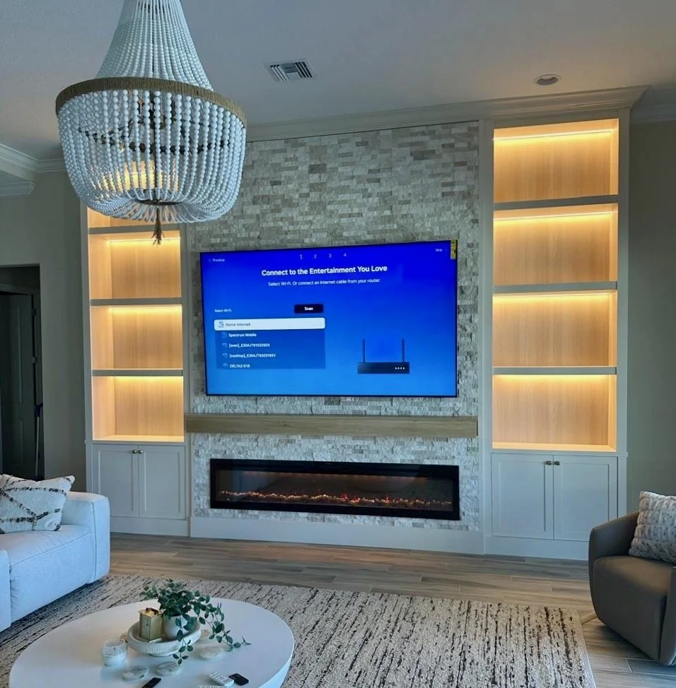 Built-in entertainment center with illuminated niches, stone accent wall, large TV and fireplace