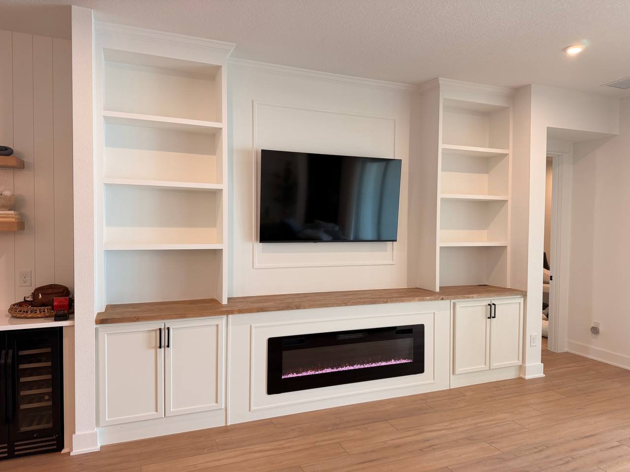 Wide view of a Signature-style built-in entertainment wall in Tampa with open shelves, shaker cabinets, mounted TV, wood countertop, and fireplace