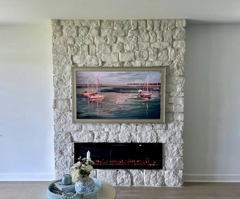 Front view of a custom white stone fireplace wall with a wide electric fireplace and framed marina artwork in a Punta Gorda living room.