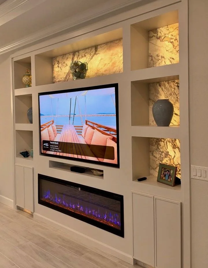 Angled view of a Tampa media wall featuring backlit stone-look niche panels, integrated TV, and electric fireplace.