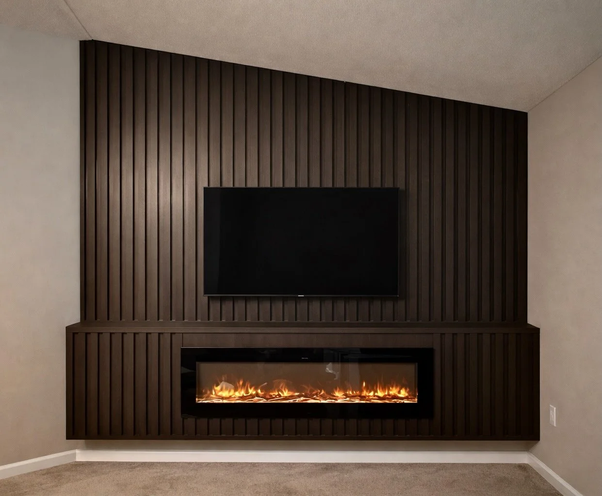 Living room with a wall-mounted flat-screen TV above a modern electric fireplace with flames, set against a dark wooden paneled feature wall.